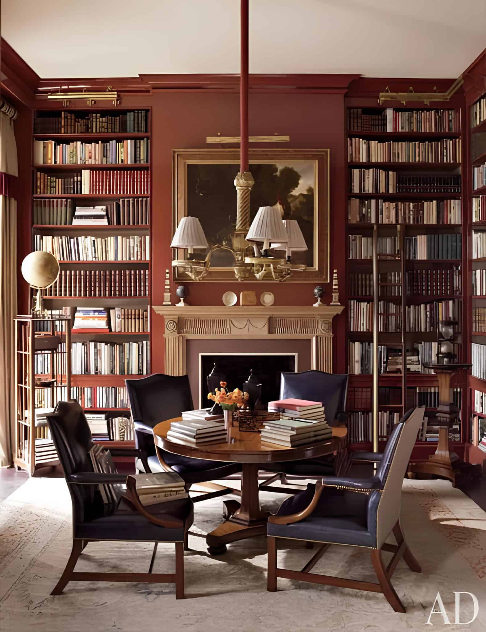 Classic red home library with fireplace, round table and leather chairs