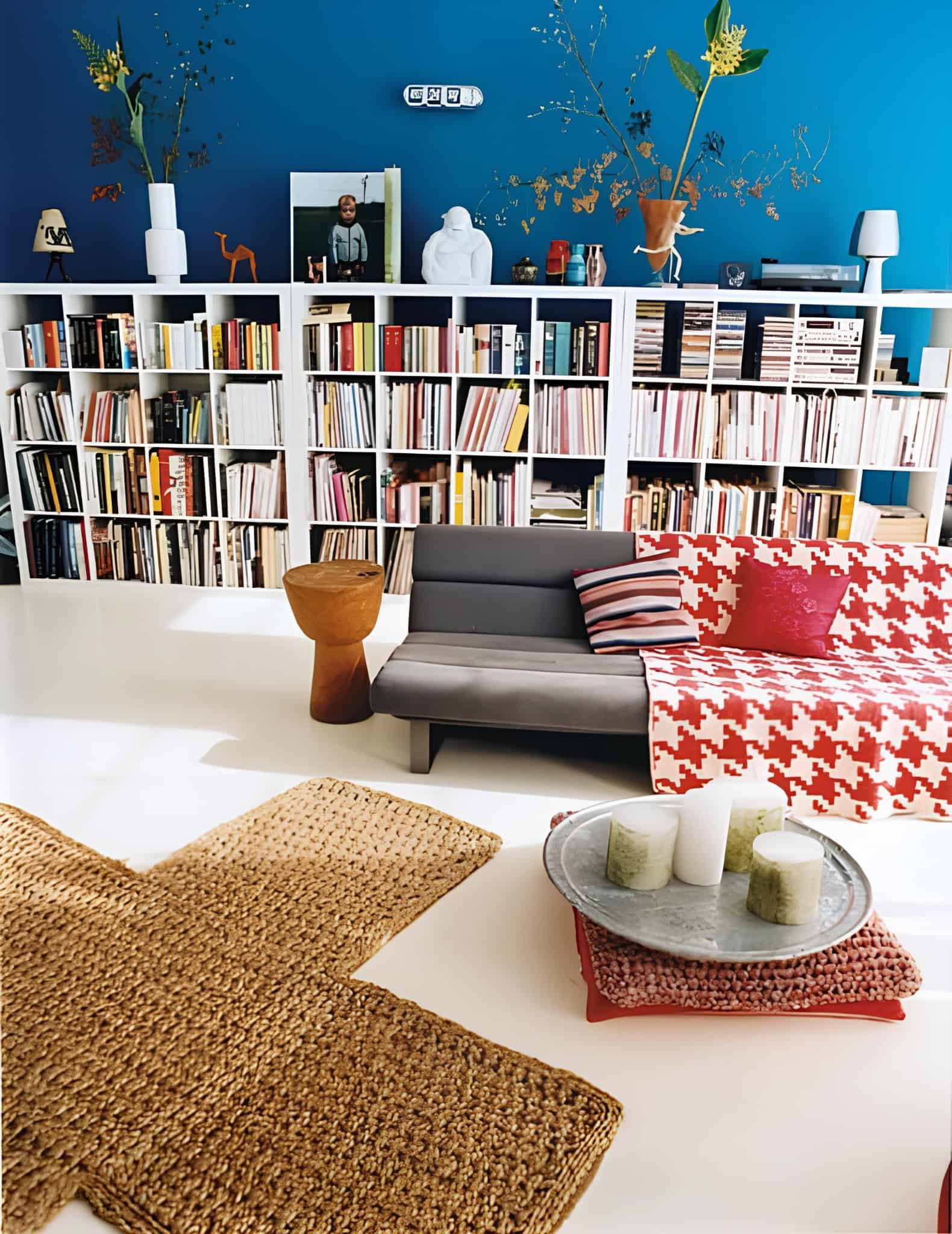 Colorful modern home library with bright blue wall, white shelves and vibrant decor