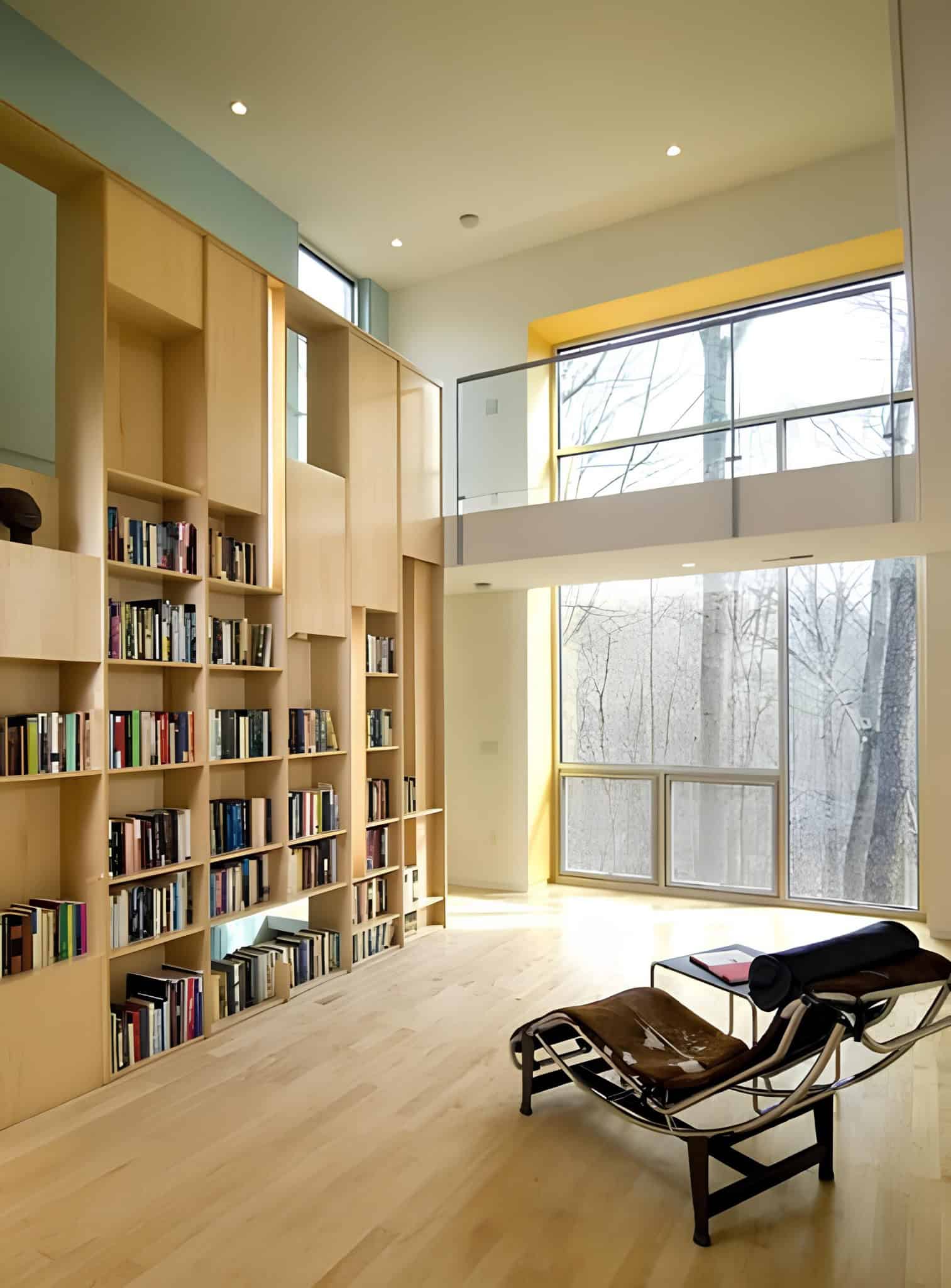 Double-height home library with tall shelves, large windows and modern chaise lounge