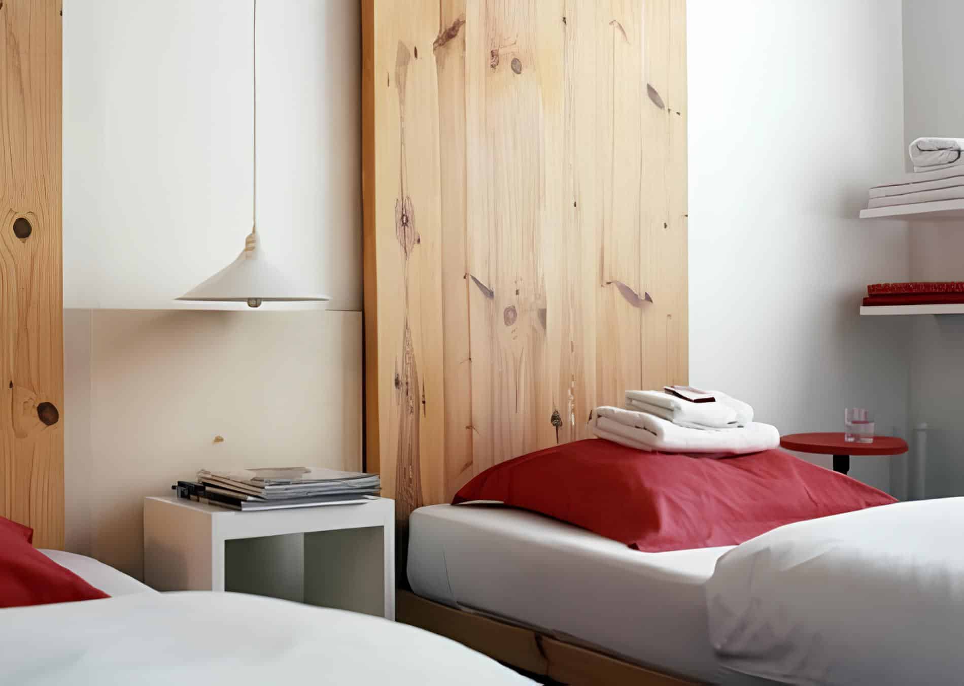 Twin beds with red pillows and wood accents in a minimalist design