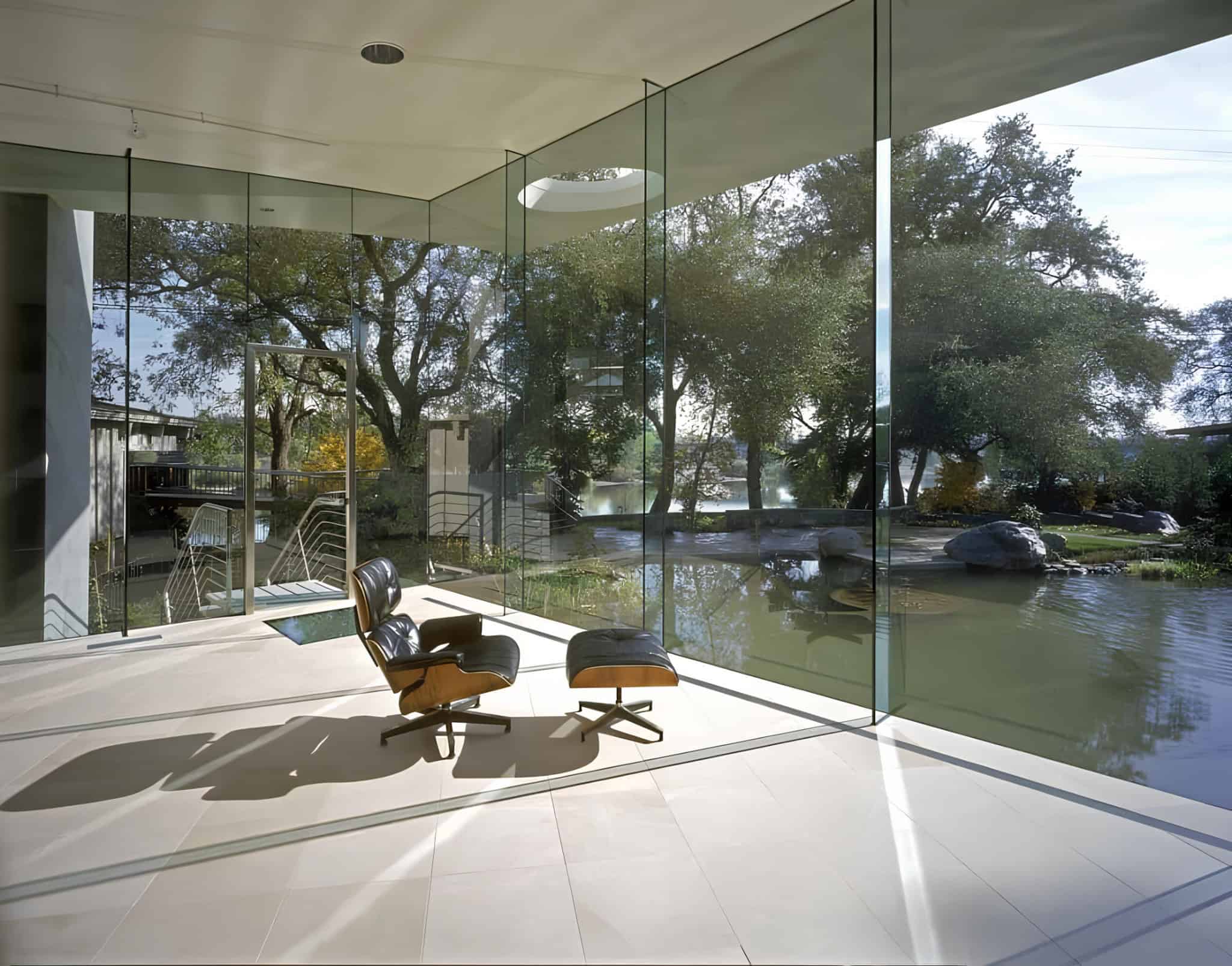 Relaxation Chair Waterfront View Iconic Eames lounge chair facing large windows with view of lake and garden.