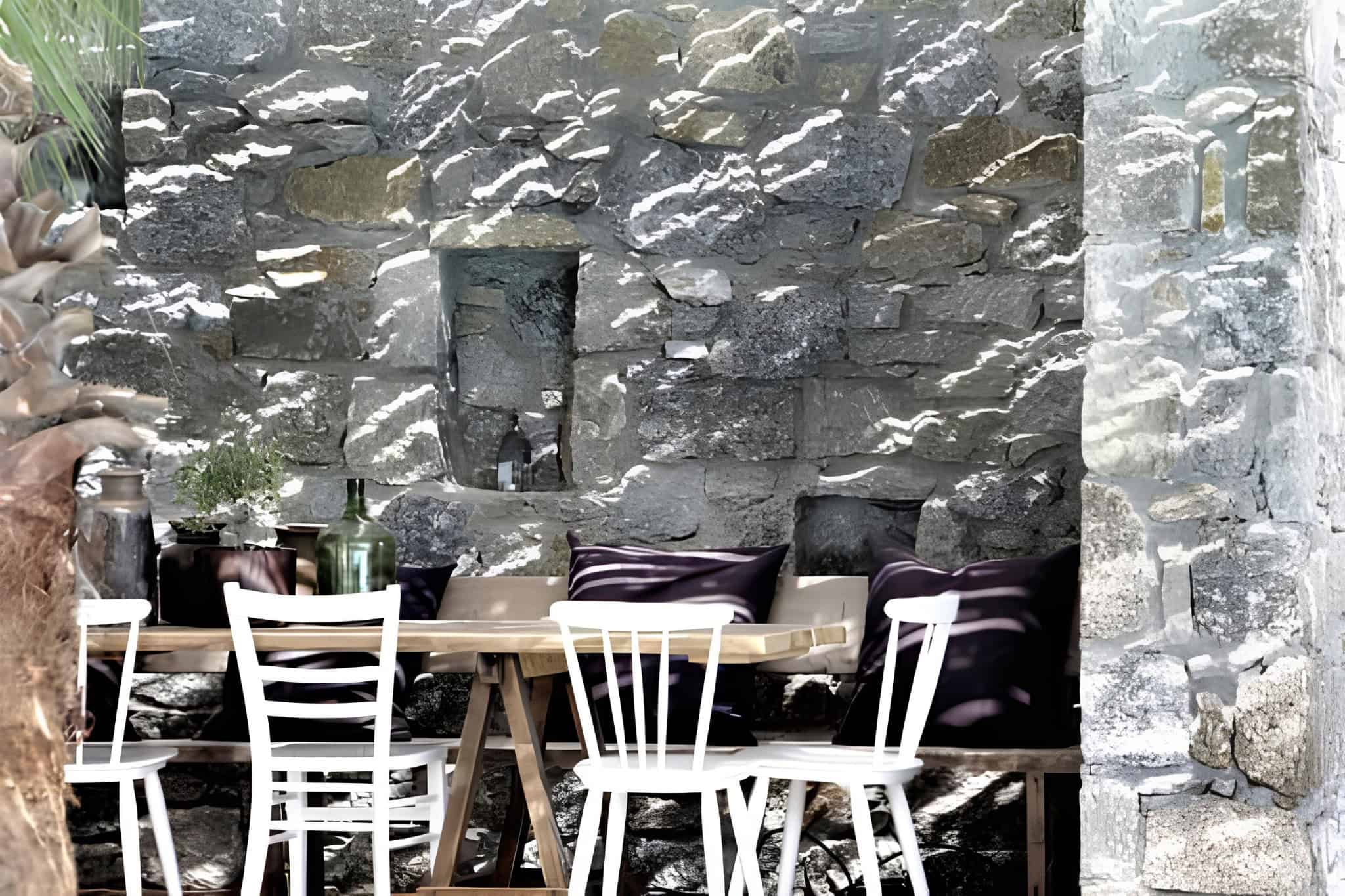 Rustic Stone Wall Dining Nook Charming outdoor nook with a stone wall backdrop and wooden dining setup.