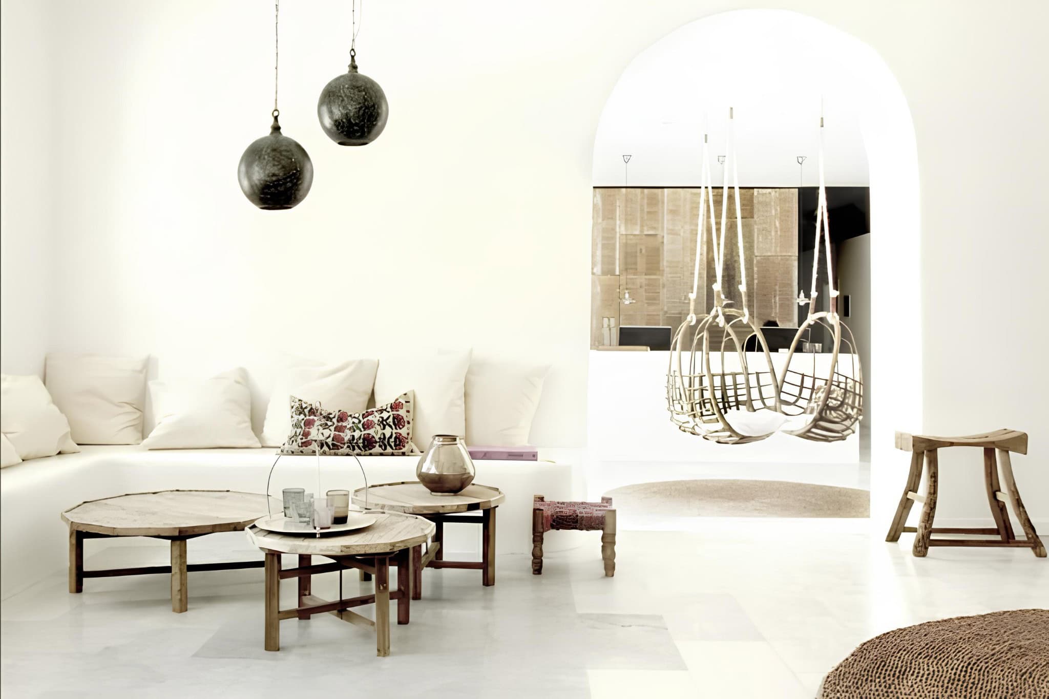 White Interior Hanging Chairs Round Tables Neutral-toned living space with hanging chairs and round wooden tables.