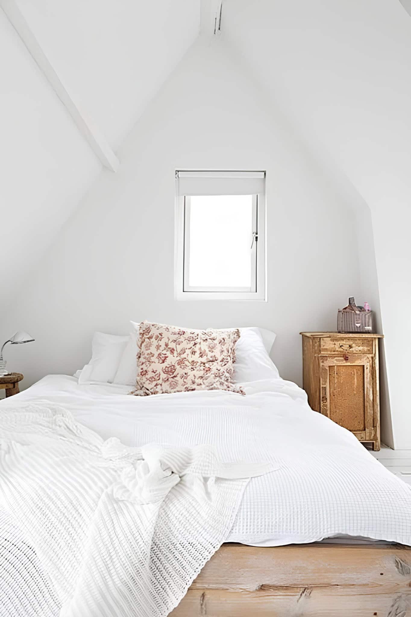 Attic White Bedroom with Floral Throw Pillow Attic-style white bedroom with sloped ceiling and rustic wood elements