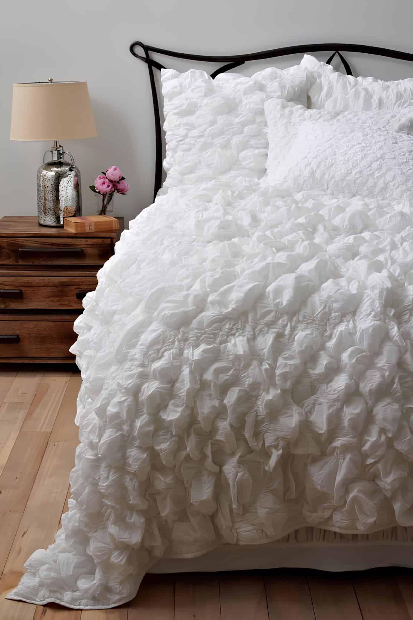 Elegant Ruffled White Bedding on Wood Bed White ruffled bedding with wooden nightstand and silver lamp