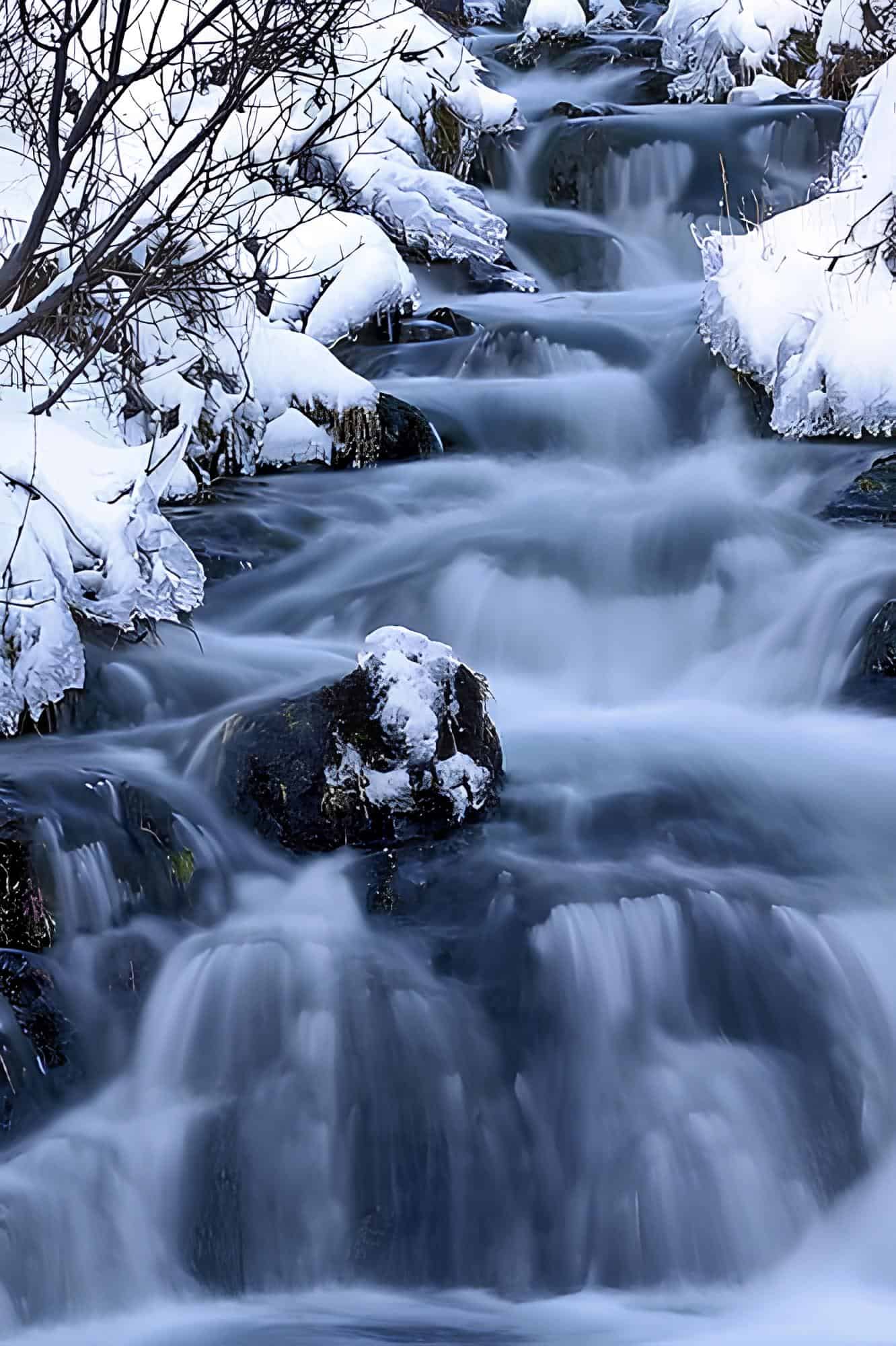 Frozen Winter Stream with Snowy Rocks Snow-covered rocks and icy stream in a tranquil winter landscape