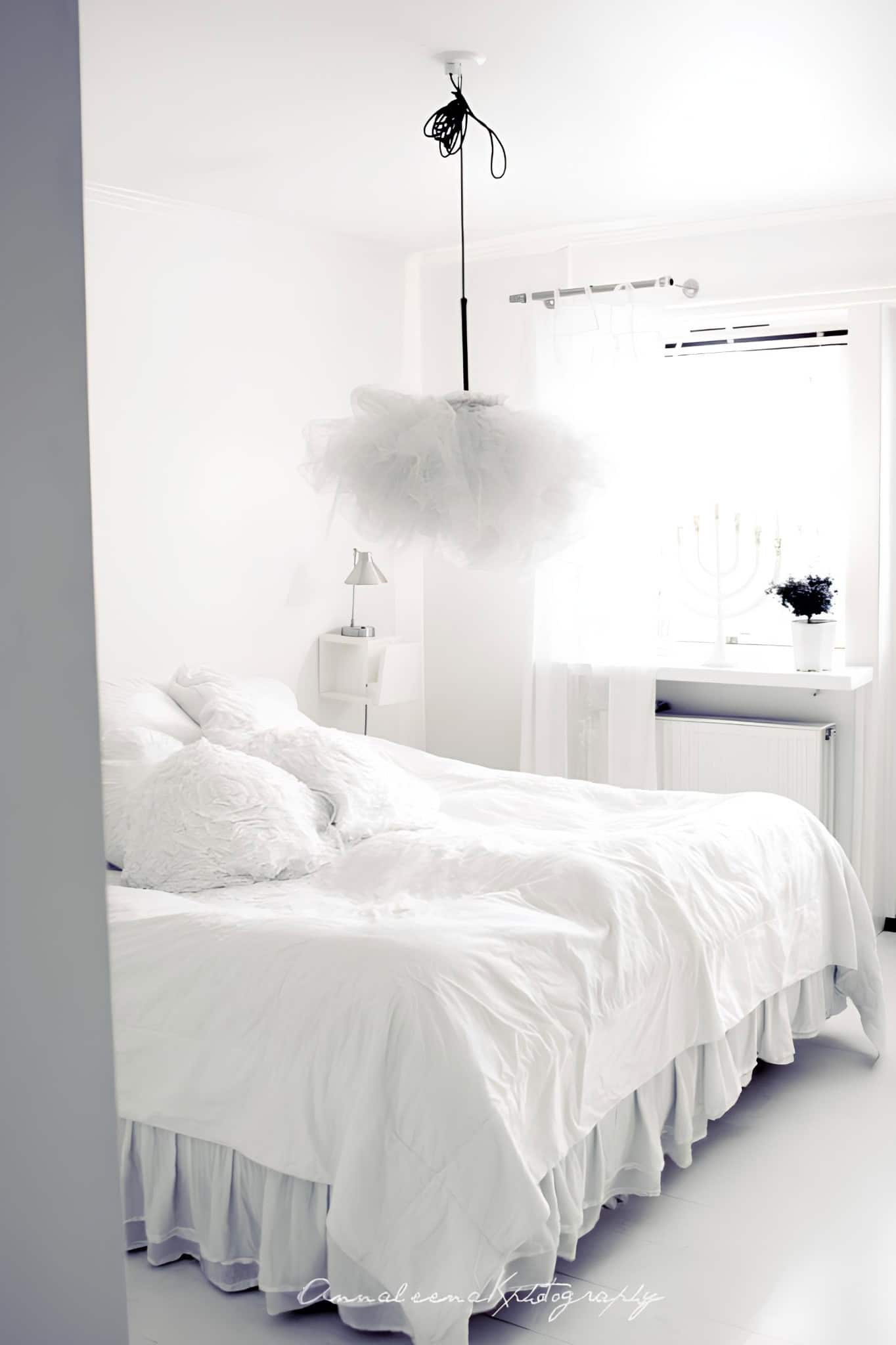 Romantic White Bedroom with Fluffy Pendant Light All-white bedroom with whimsical pendant light and tufted pillows