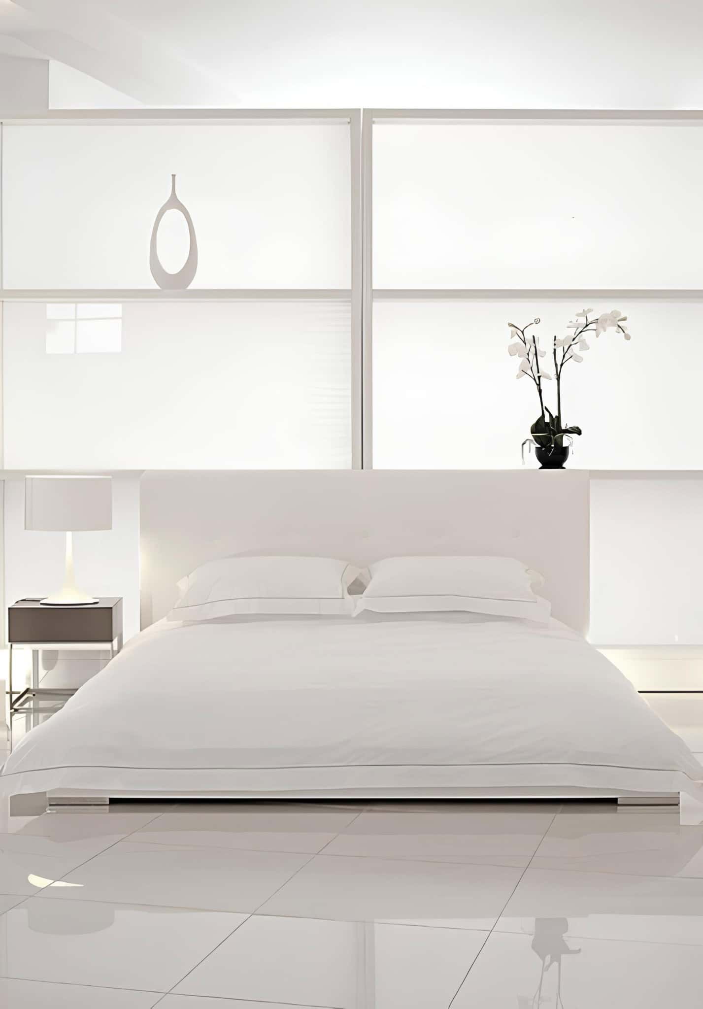 Sleek Modern Bedroom with Orchid and White Bed Minimalist white bedroom with low platform bed, nightstand and orchid