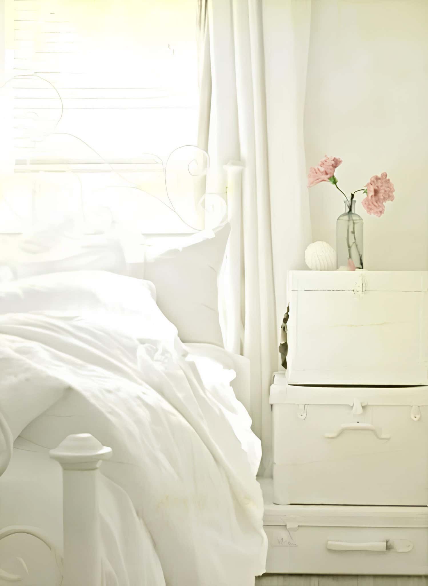 Sunlit White Bedroom with Pink Flowers Bright white bed next to a vintage chest with pink flowers