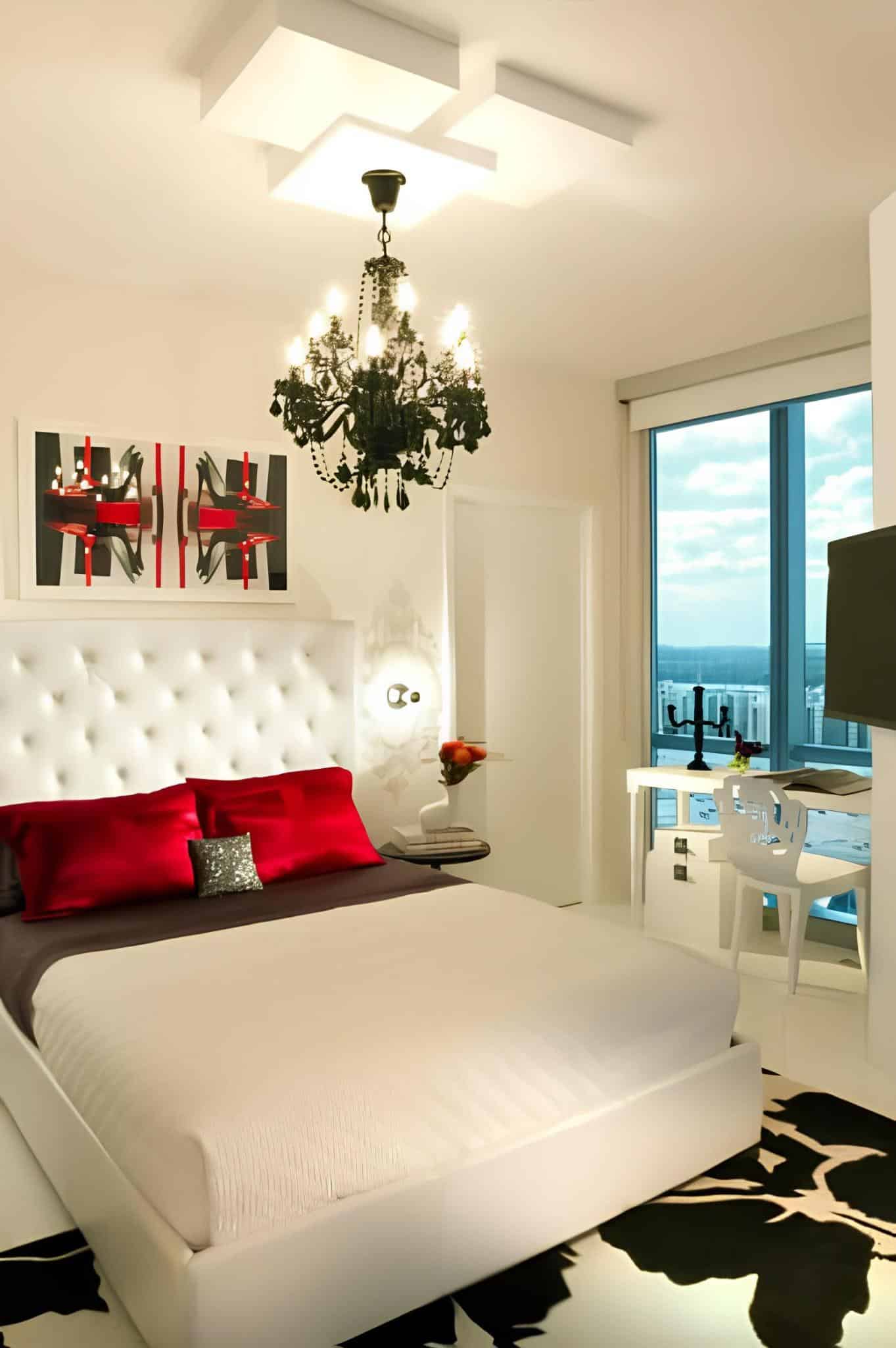 White bedroom with red pillows, black chandelier, and dramatic accents
