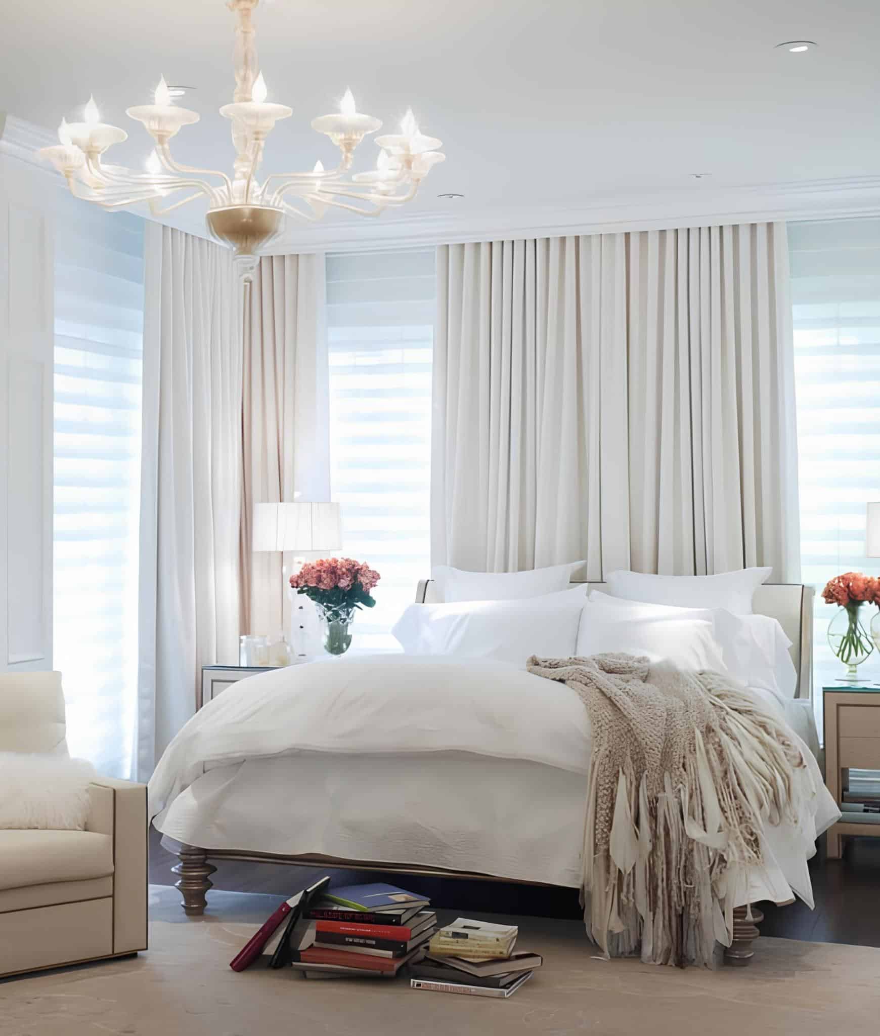 Bright bedroom with white curtains, chandelier, and stacks of books