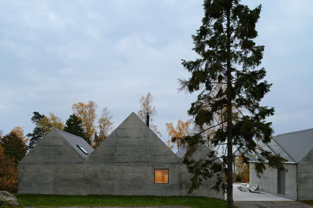 Contemporary concrete house with unique angular roof design and large windows, nestled in a natural landscape with tall trees, modern architecture, eco-friendly construction, innovative residential design, and minimalist style.