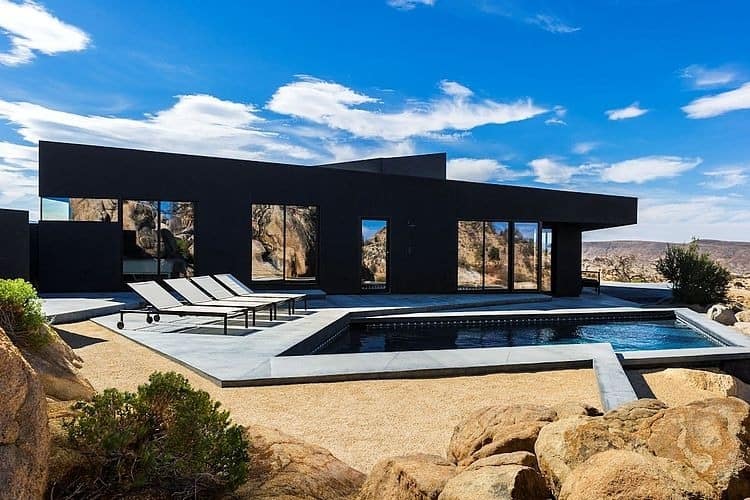 Contemporary black minimalist house with infinity pool and desert landscape, showcasing modern architecture and outdoor living design.