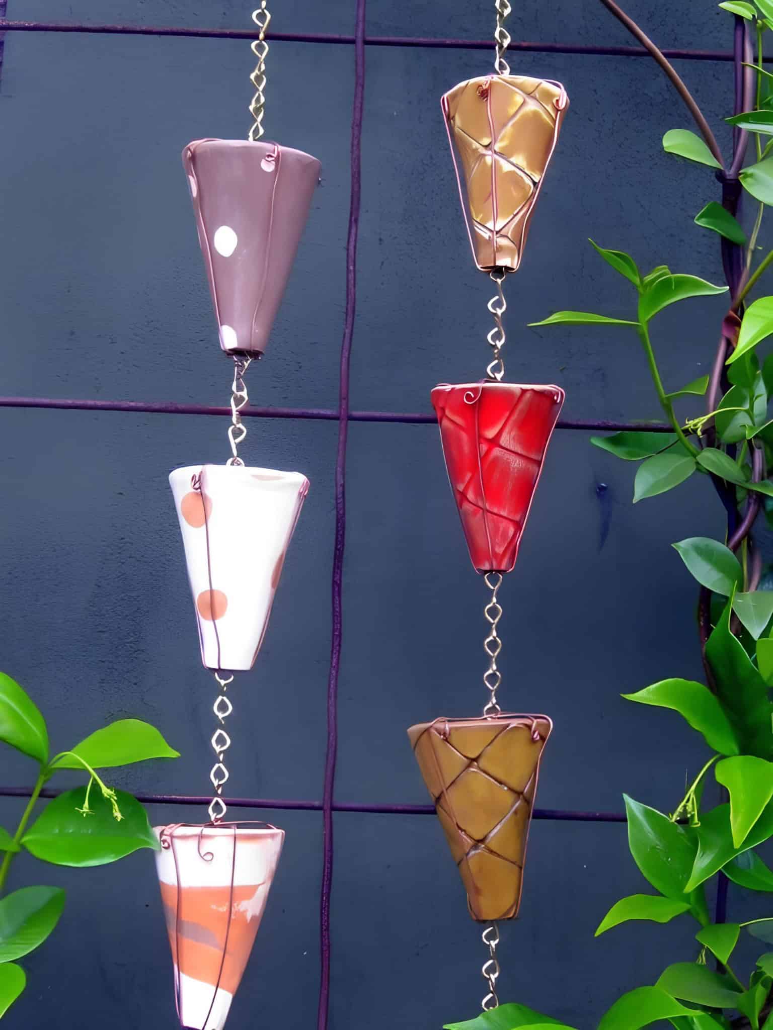 Colorful cone-shaped rain chain cups hanging against a dark wall with greenery