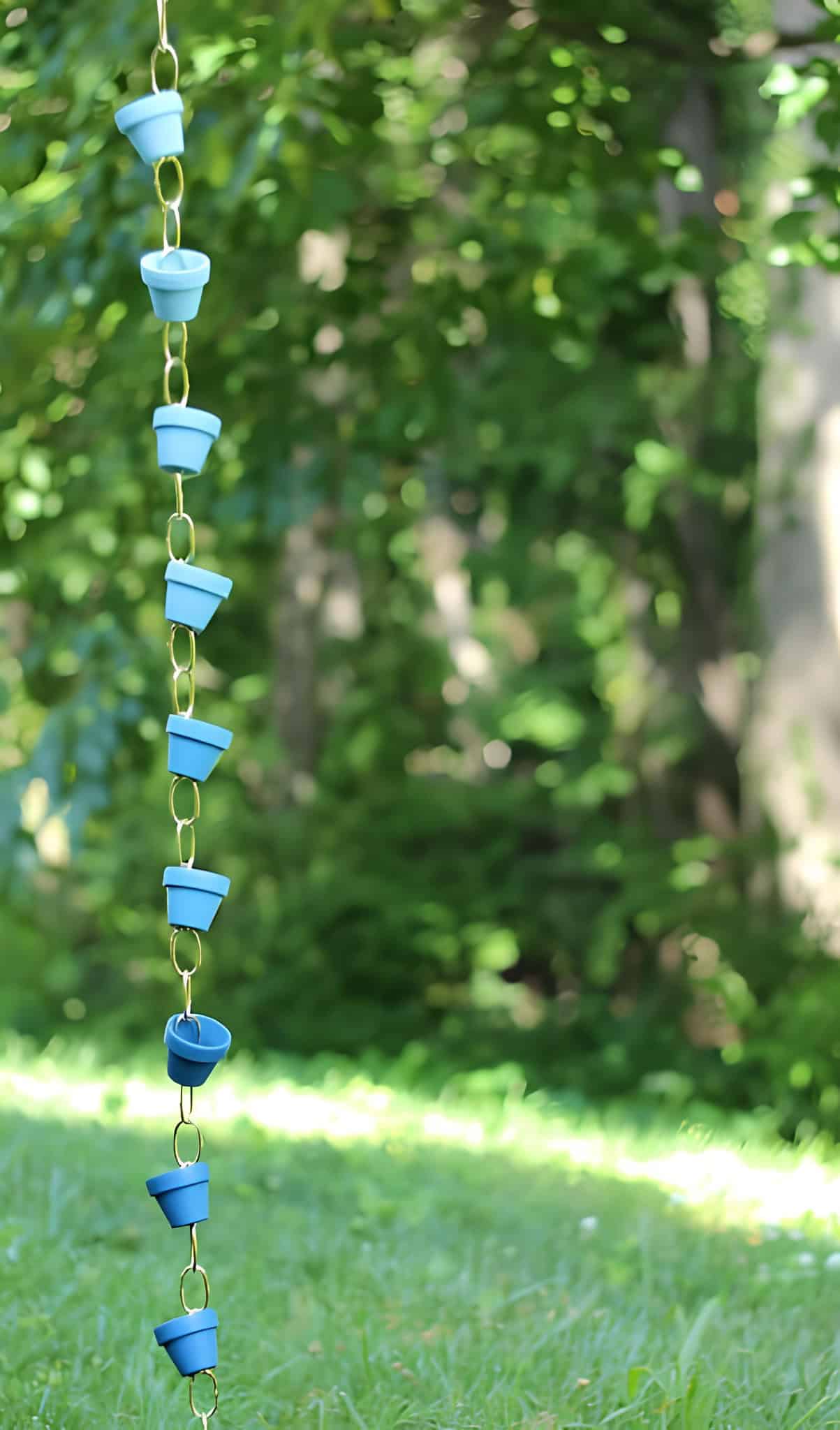 Blue miniature flowerpots linked together forming a playful rain chain in a green garden