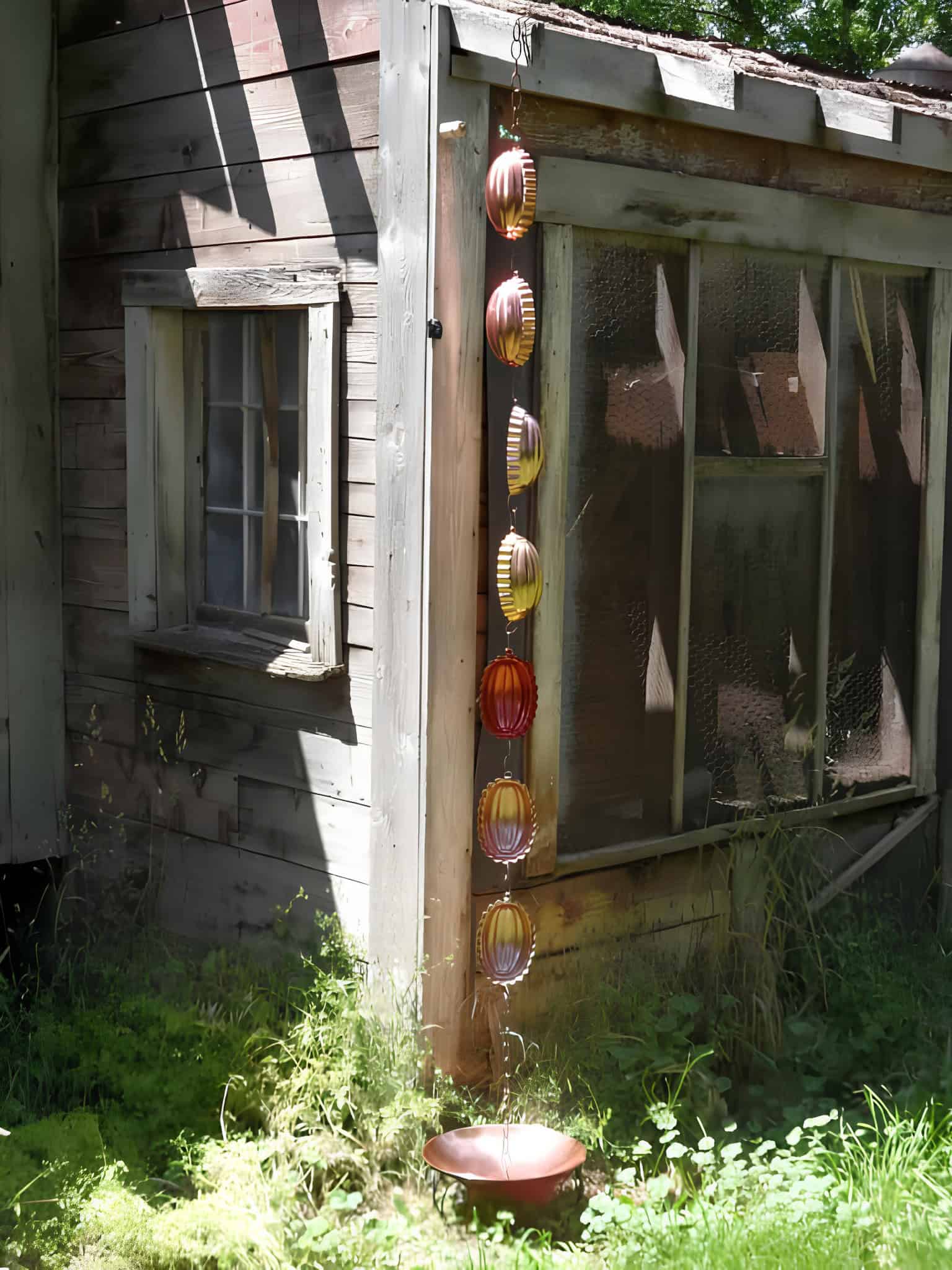 Colorful metal rain chain cups hanging by a weathered wooden shed