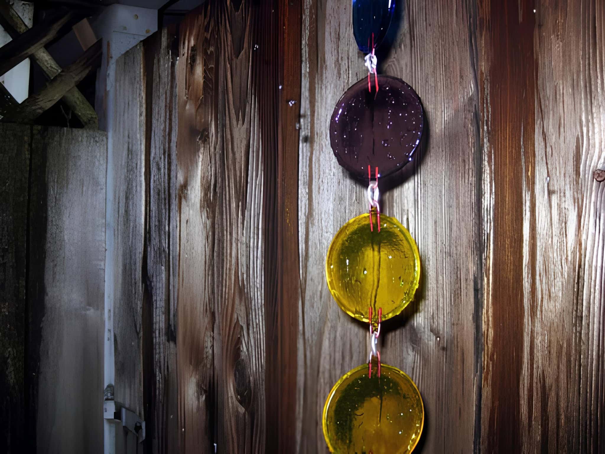 Rain chain made of colorful glass discs hanging against a wooden fence