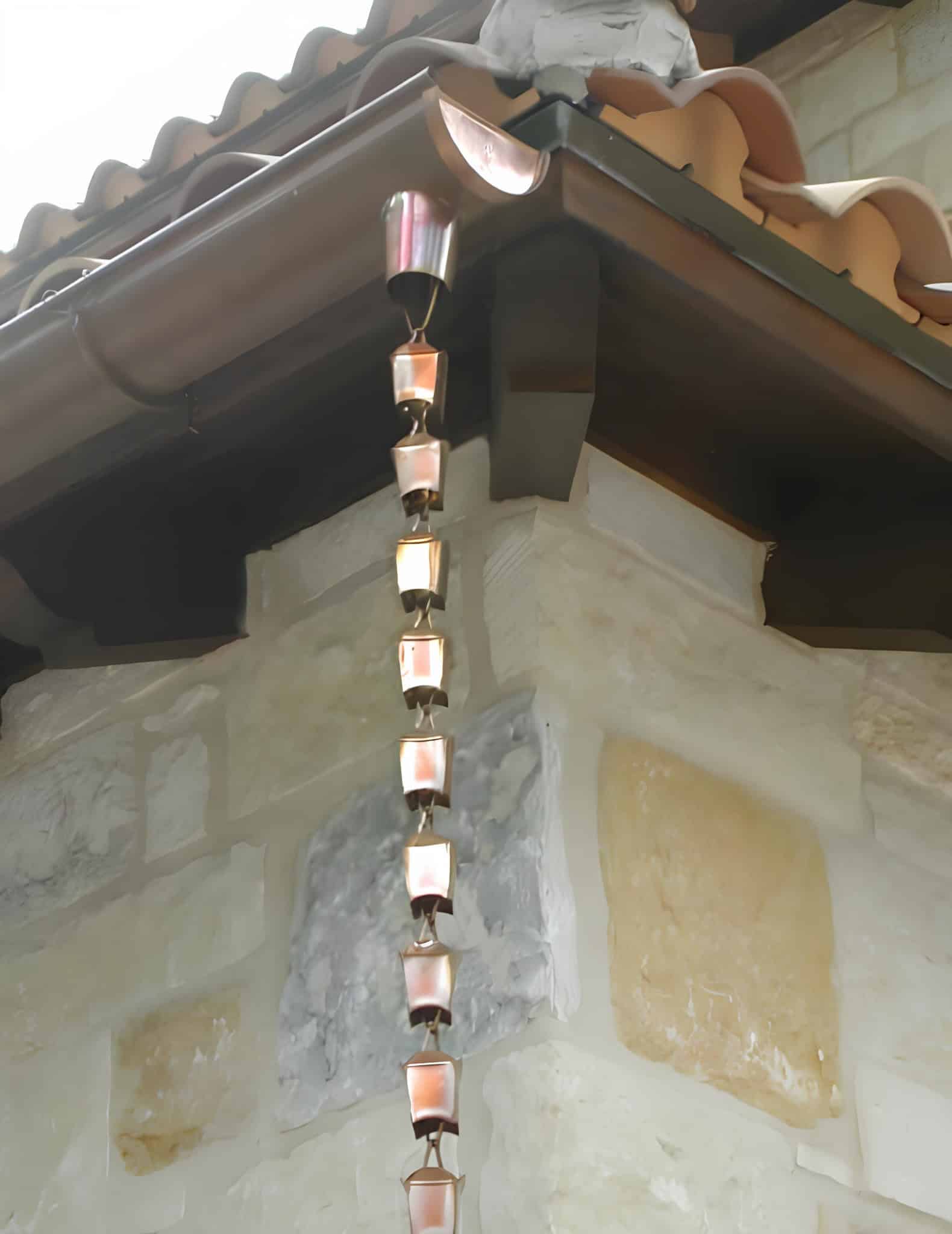 Copper rain chain hanging from a gutter on a stone house exterior