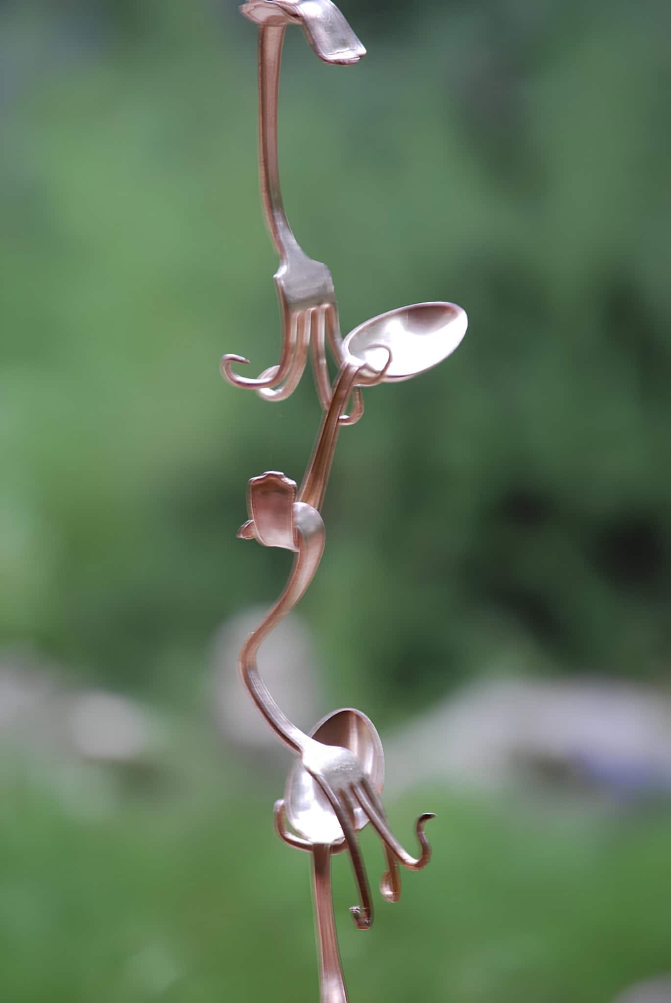Handcrafted copper spoon rain chain hanging in a garden