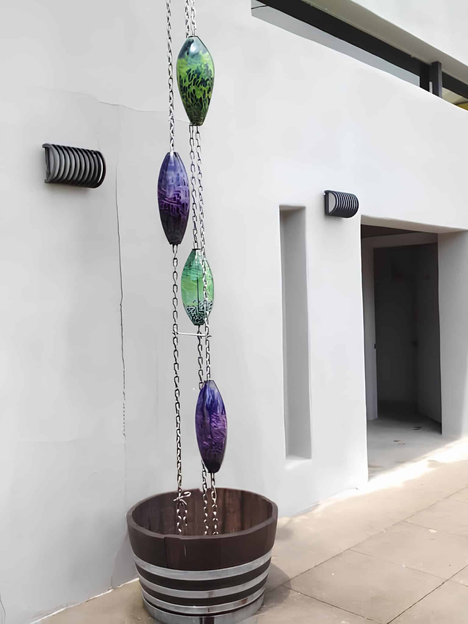 Decorative glass vessel rain chain installed outside a modern white house