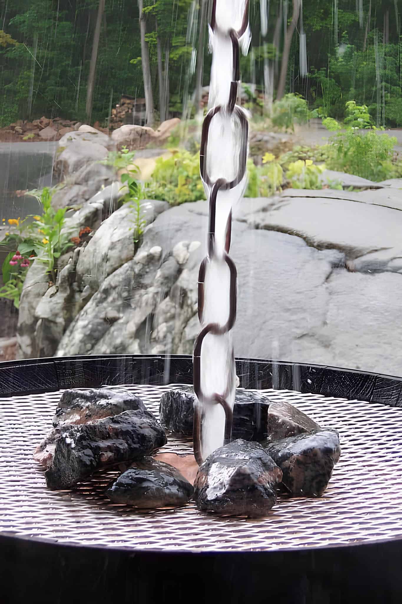 Water rushing heavily down a metal chain into a rock-filled basin outdoors