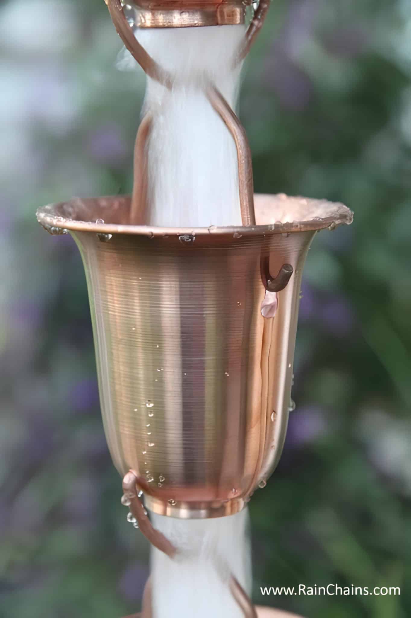 Close-up of a large copper rain chain cup with water rushing through it
