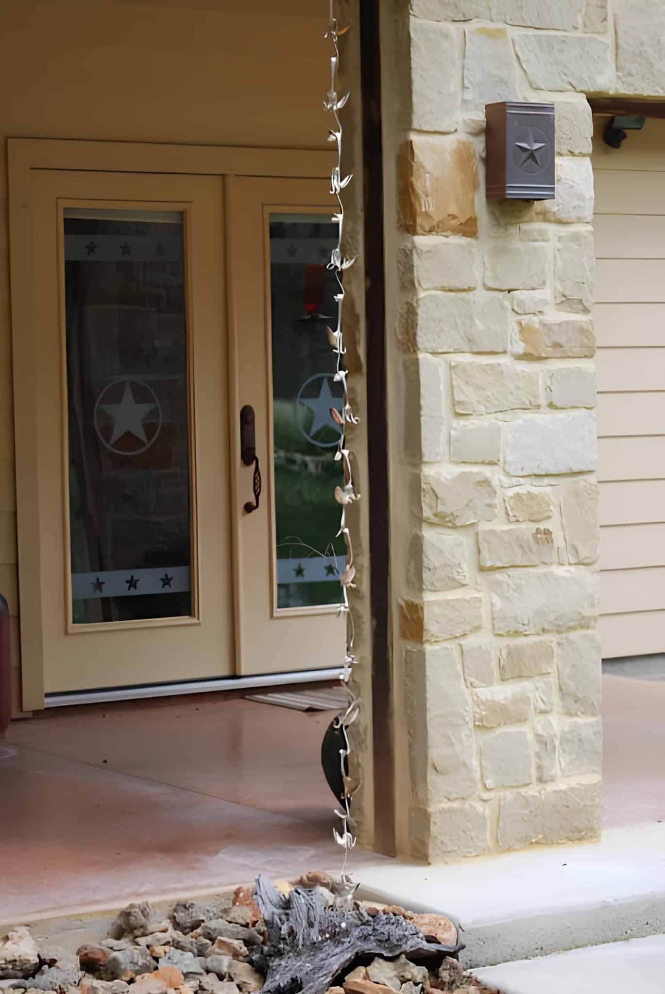 Copper spoon rain chain hanging from a porch roof near a stone column