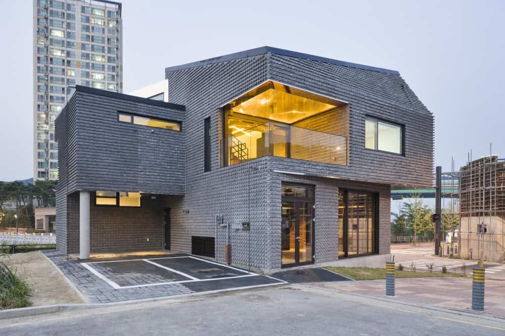 Modern black brick house with contemporary architecture, large glass windows, and a unique geometric design in an urban setting.