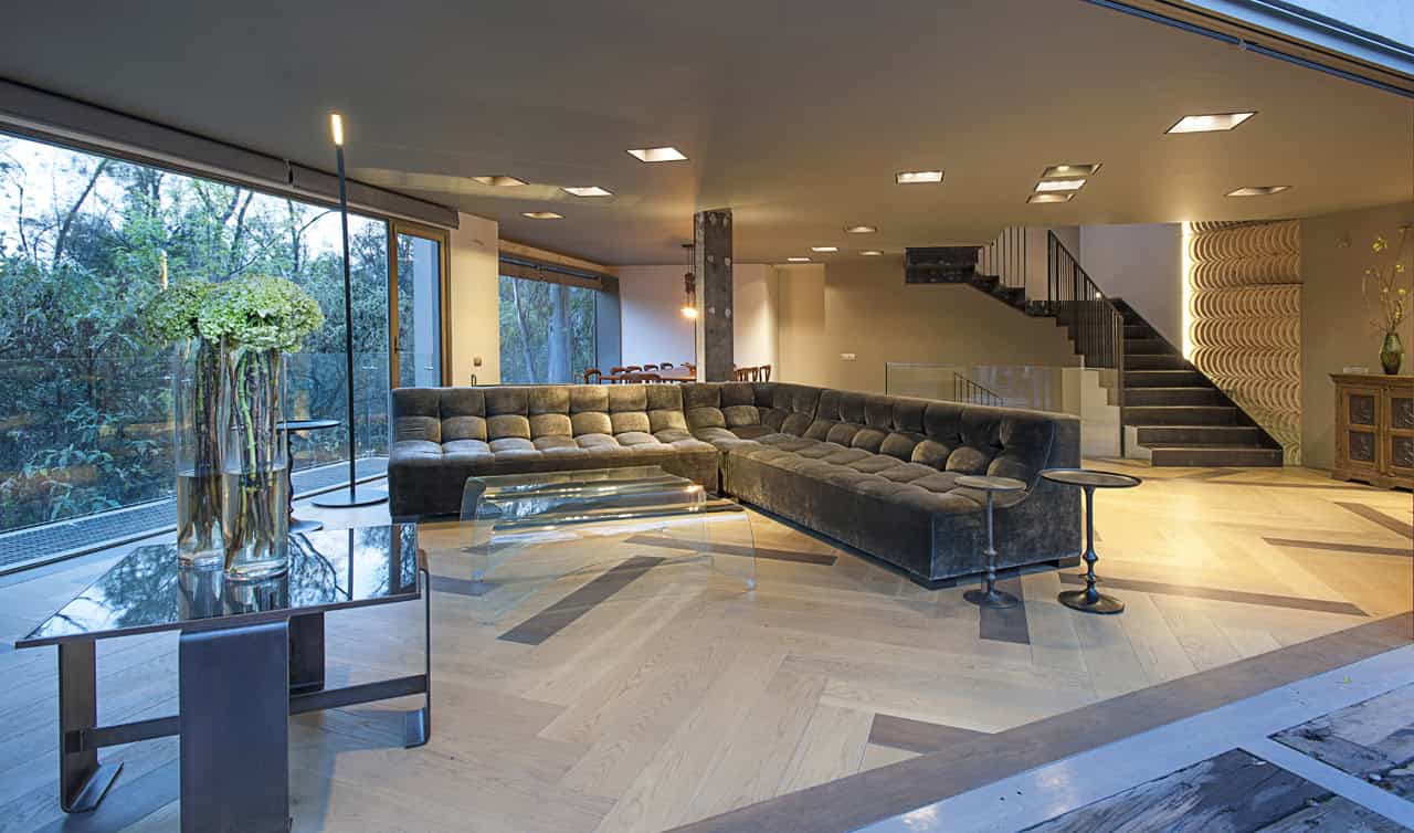 Luxurious modern living room with large floor-to-ceiling windows, sleek black sectional sofa, contemporary decor, and stylish staircase, showcasing innovative architectural design and interior art.