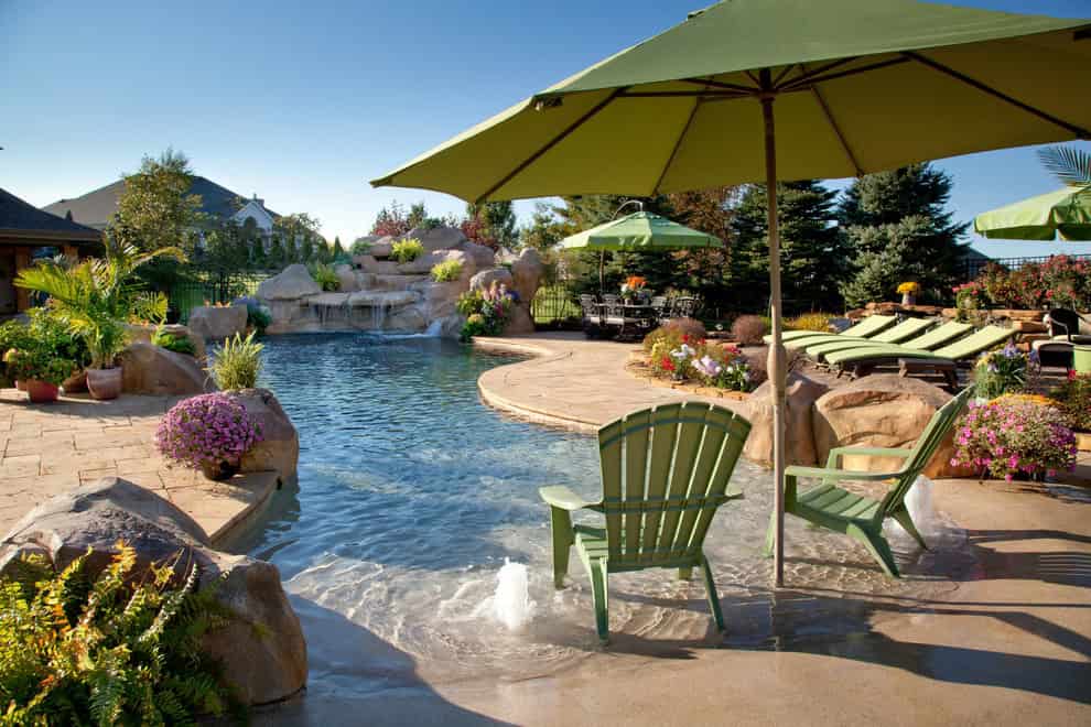 lagoon swimming pool with a vanishing edge, rock waterfall, slide, beach entry with rock accents, water geysers and a large travertine patio Source