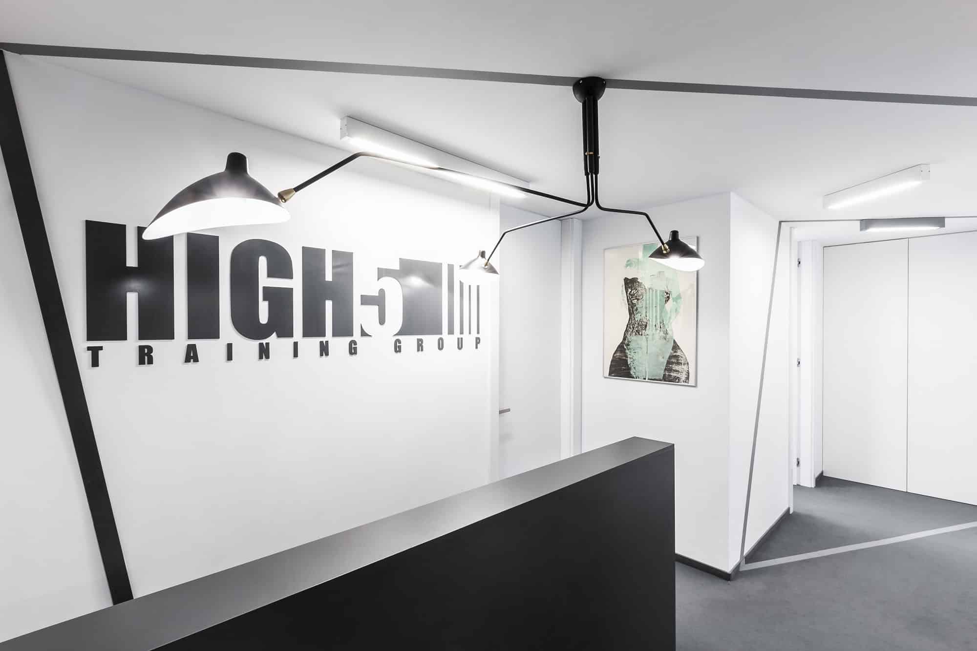 Modern gym reception area with sleek black and white design, featured lighting, and motivational signage for high-intensity training groups.