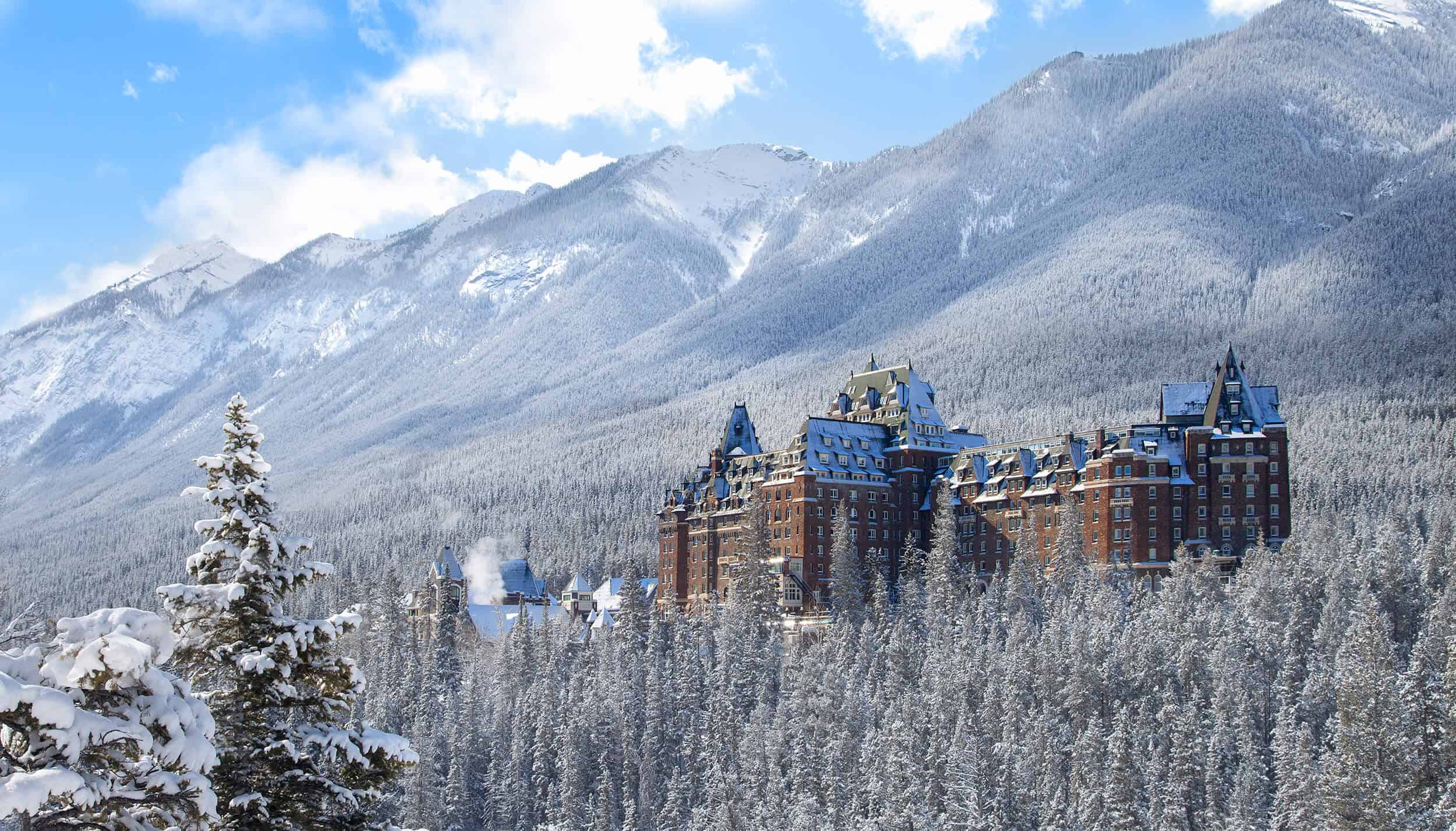 Banff Springs Hotel in Banff National Park, Canada, framed by snow-covered pine trees and Rocky Mountain peaks during winter.