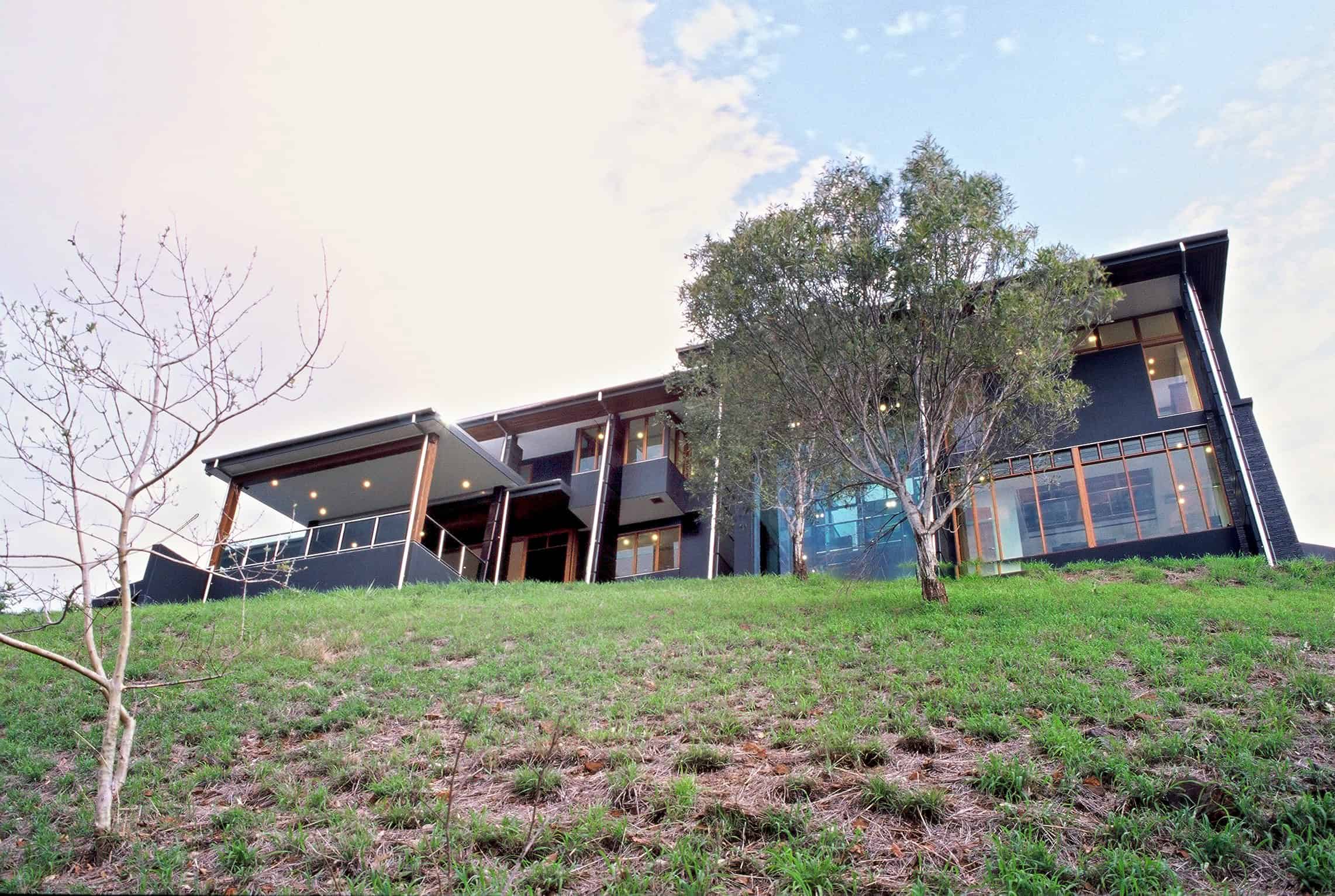 Modern black architectural house with large glass windows on a grassy hillside, featuring contemporary design and sleek lines.