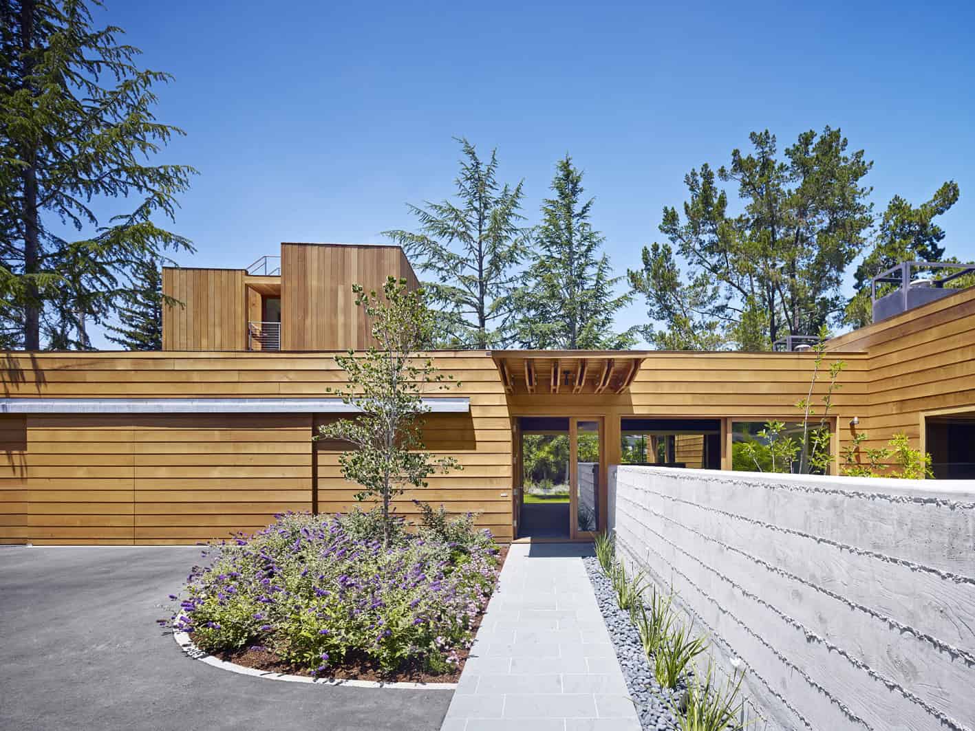 Modern eco-friendly house with wooden exterior and clean architectural design surrounded by lush trees and landscaped garden.