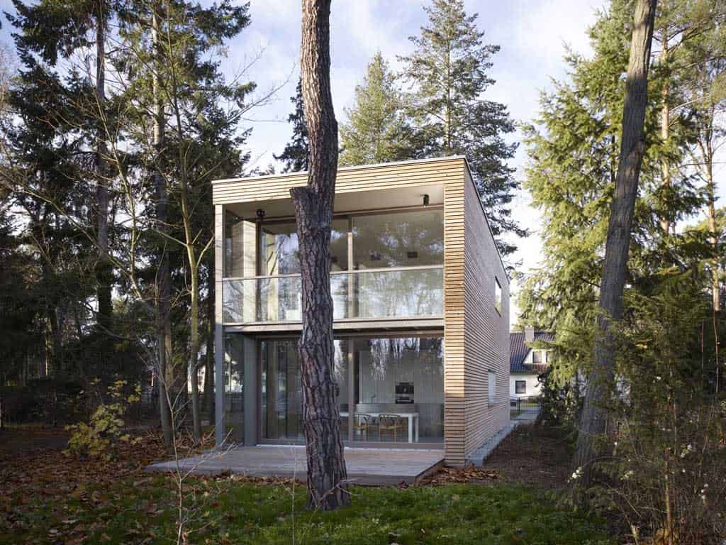 Modern two-story house with extensive glass windows and wooden exterior in a wooded setting, showcasing contemporary architecture and design.