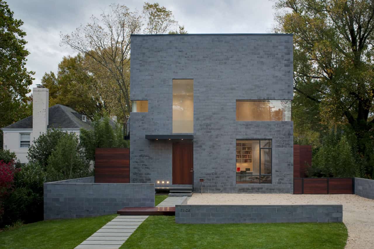 Contemporary modern house with minimalist design, gray brick exterior, large glass windows, and landscaped front yard, showcasing innovative architecture and stylish curb appeal.
