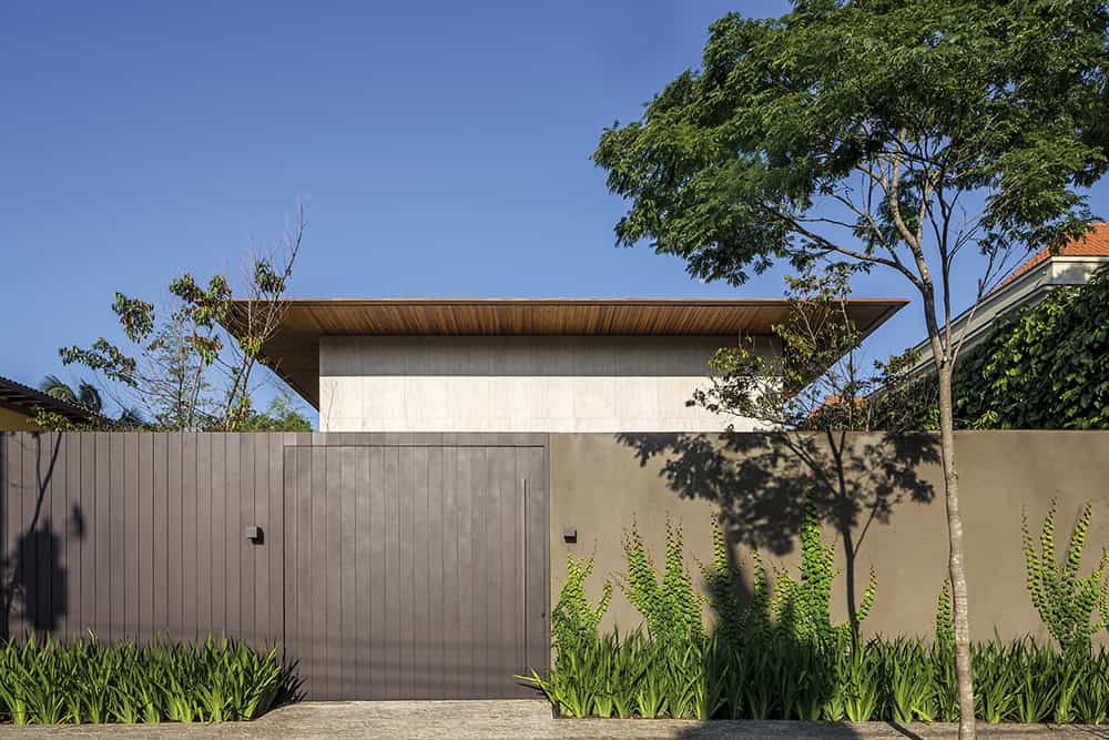 Modern minimalist house exterior with sleek concrete fence and lush greenery, showcasing contemporary architecture and landscaping design.