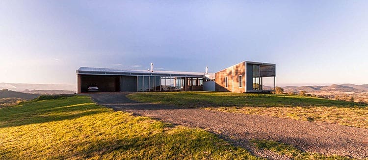 Modern minimalist house with large glass windows and flat roof in a scenic landscape architectural design.