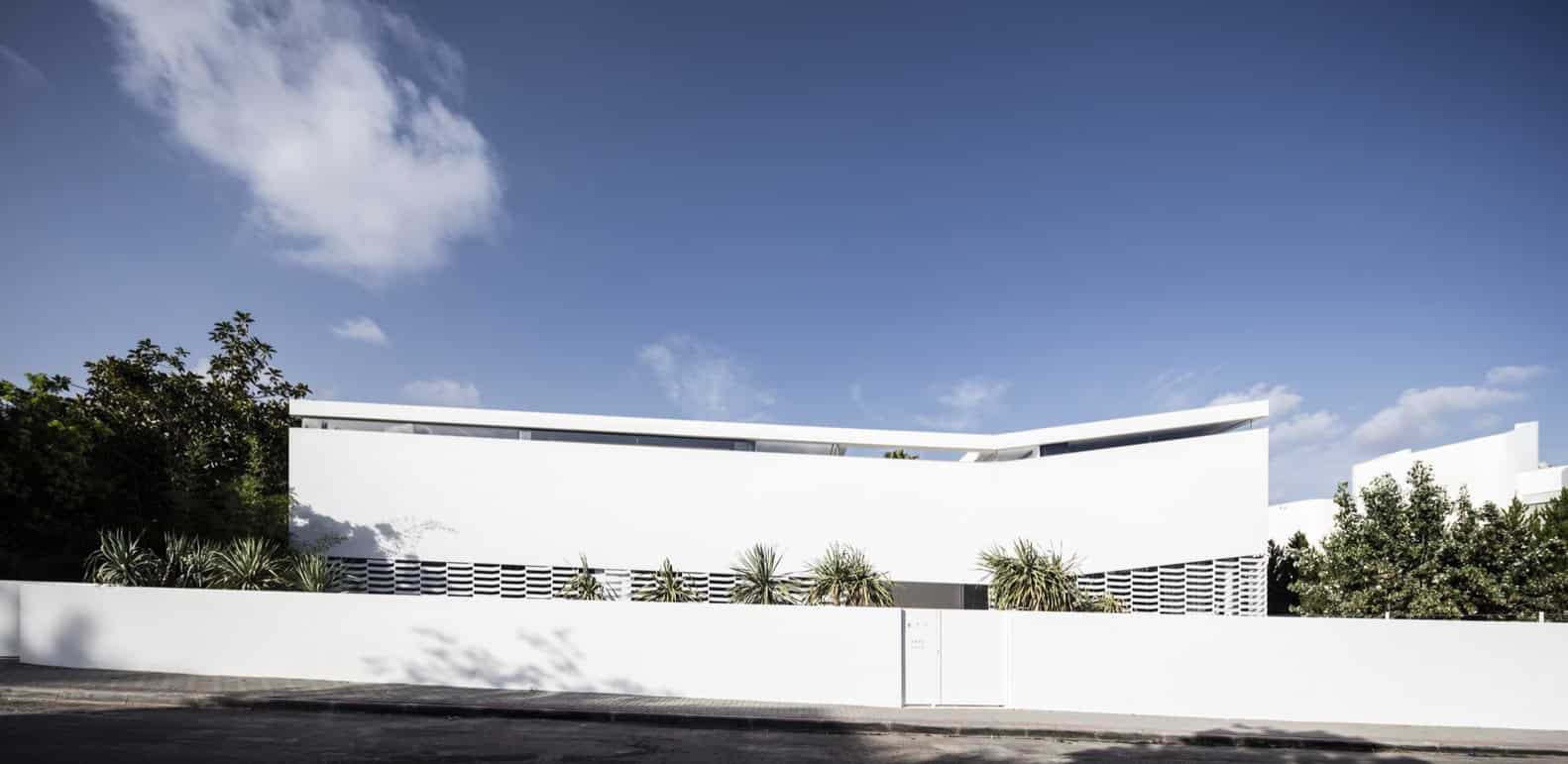 Modern minimalist white residential building with sleek curves and lush landscaping, showcasing contemporary architecture and innovative design.