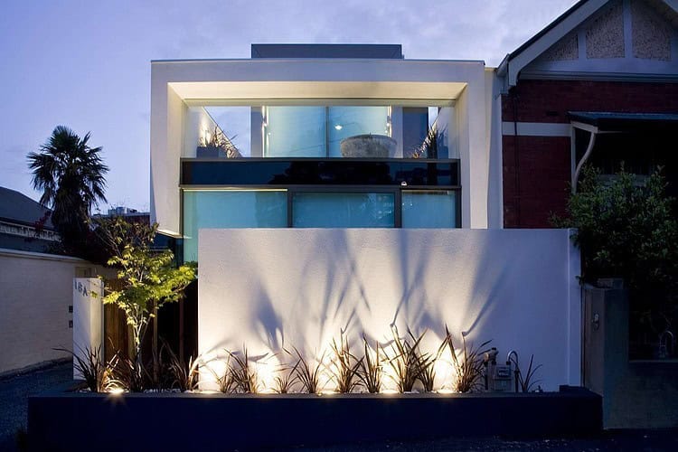 Modern minimalist house with sleek architectural design and large glass windows, illuminated at night with landscape lighting for curb appeal.