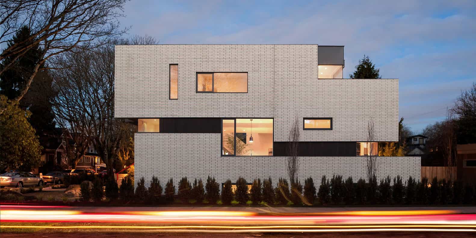 Modern minimalist white brick residential building with large windows at dusk, showcasing contemporary architecture and innovative urban design.