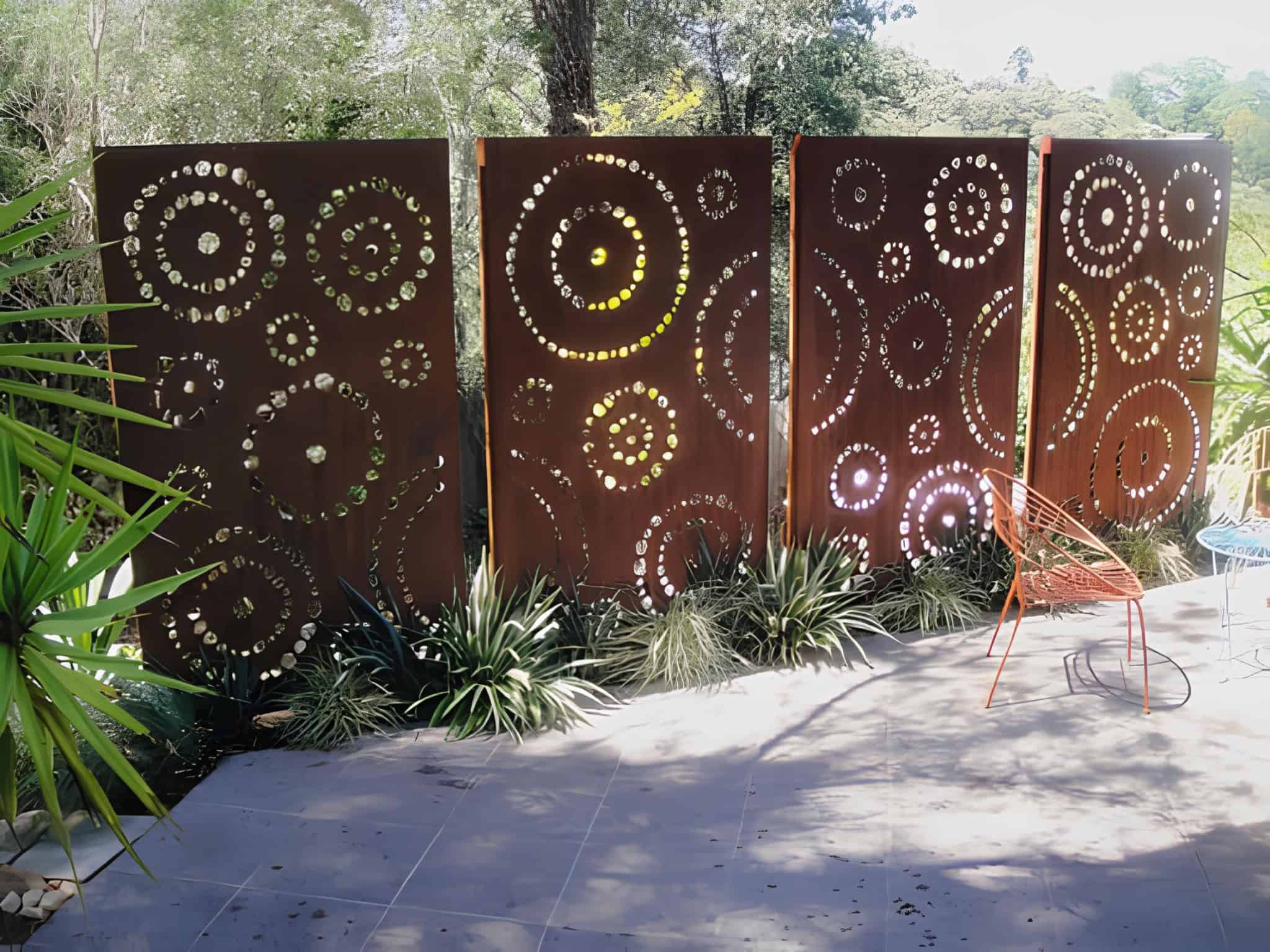 Rust-colored corten steel privacy panels with decorative cutouts in a backyard