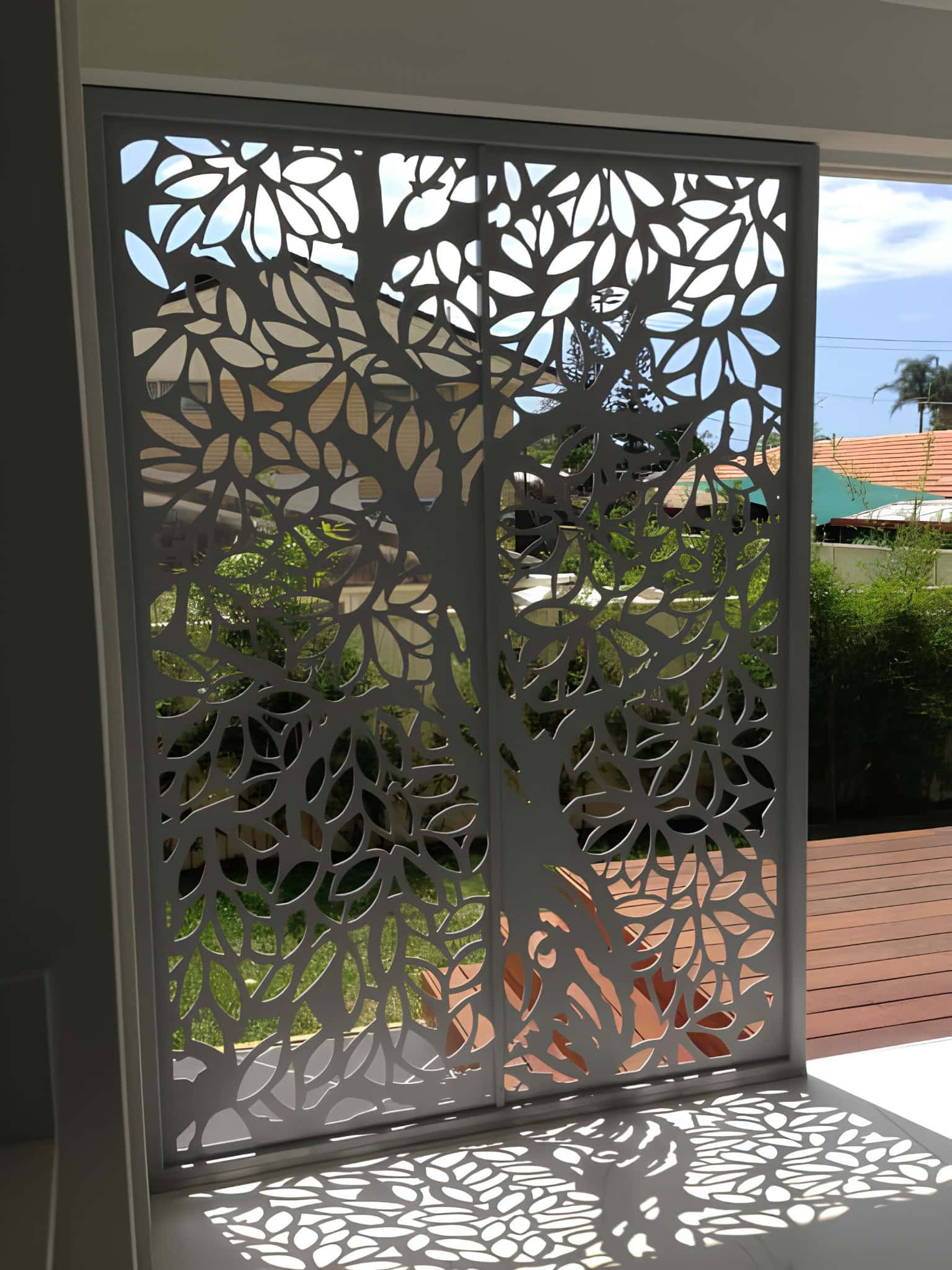 Laser-cut metal privacy panel with tree branch pattern in front of a garden