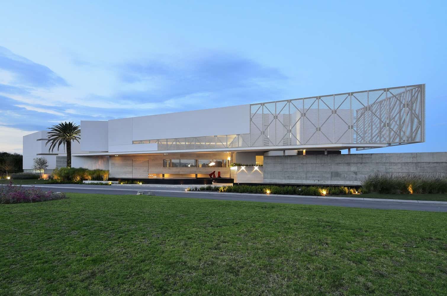 Contemporary modern house with sleek white architecture, clean lines, and unique geometric facade design, surrounded by manicured lawn and landscaped garden, showcasing minimalist luxury style.
