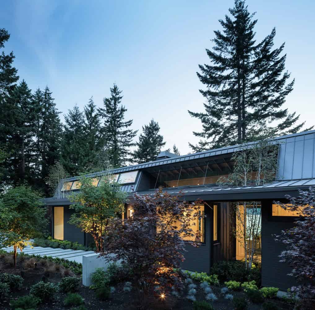 A modern house with sleek black exterior design, surrounded by lush green trees and landscaping, showcasing contemporary architecture and innovative home design in a serene natural setting.