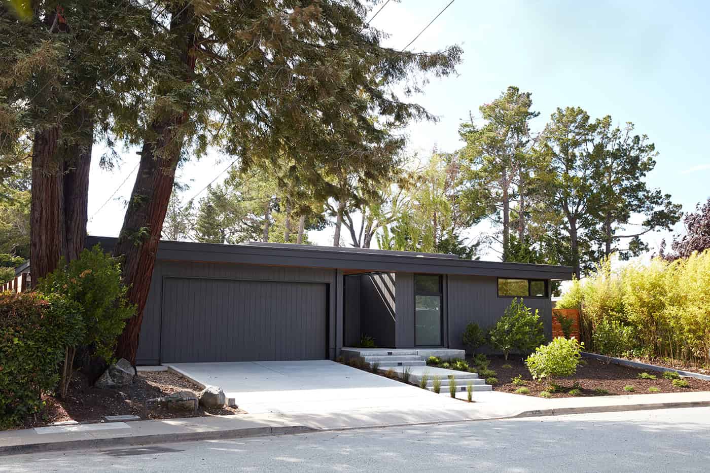 Contemporary modern house exterior with dark gray siding, sleek design, and lush landscape, showcasing innovative architecture and stylish home design.