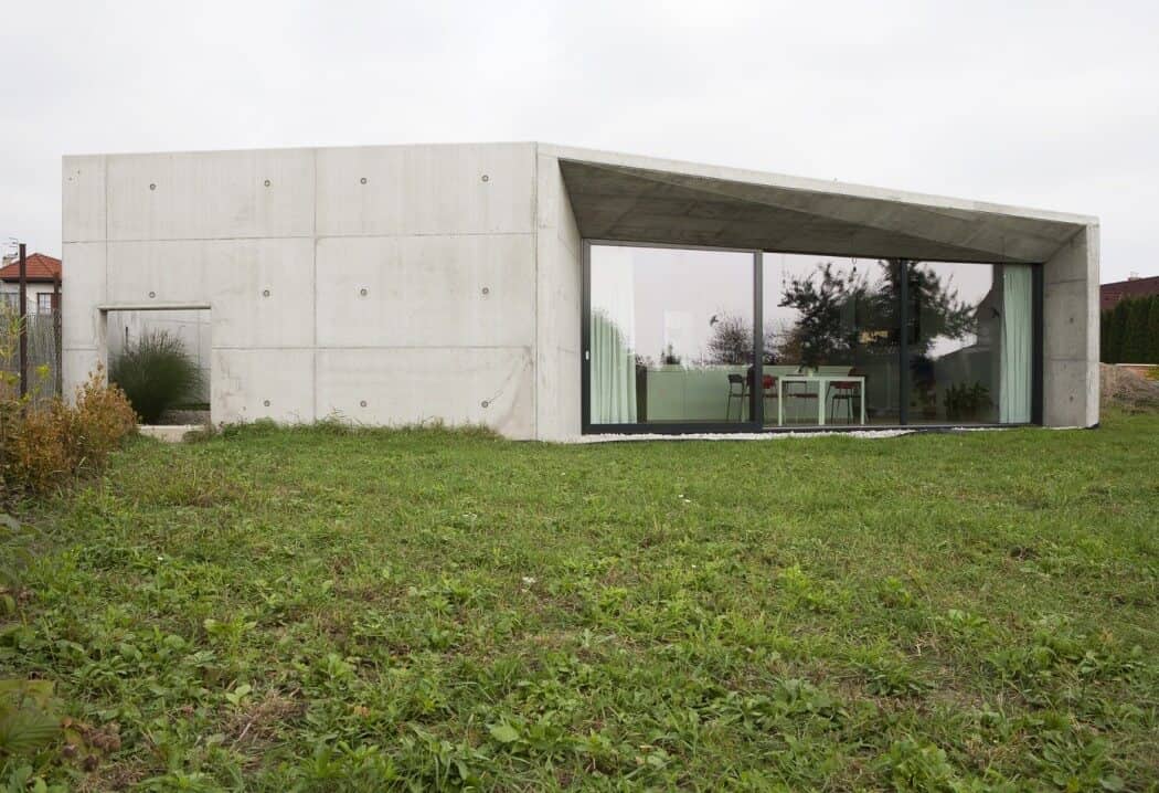 Contemporary minimalist concrete house with large glass windows, modern architecture, and sleek design on a lush green lawn, showcasing innovative residential architectural styles.