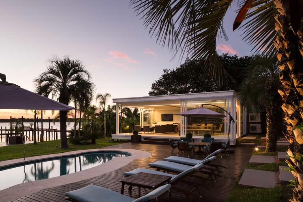 Modern waterfront poolside retreat with lush tropical landscaping and an outdoor lounge area, perfect for relaxing and entertaining at sunset.