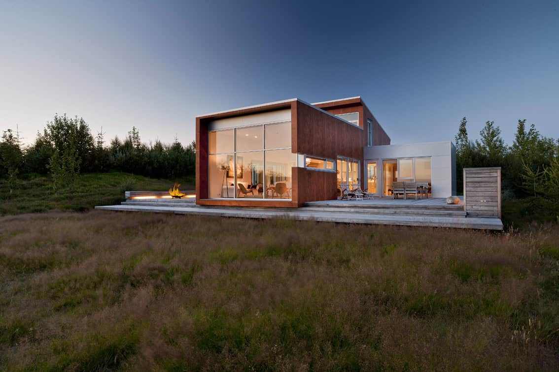 Modern minimalist house with large glass windows and wooden exterior design in a natural landscape, showcasing contemporary architecture and stylish outdoor living spaces.