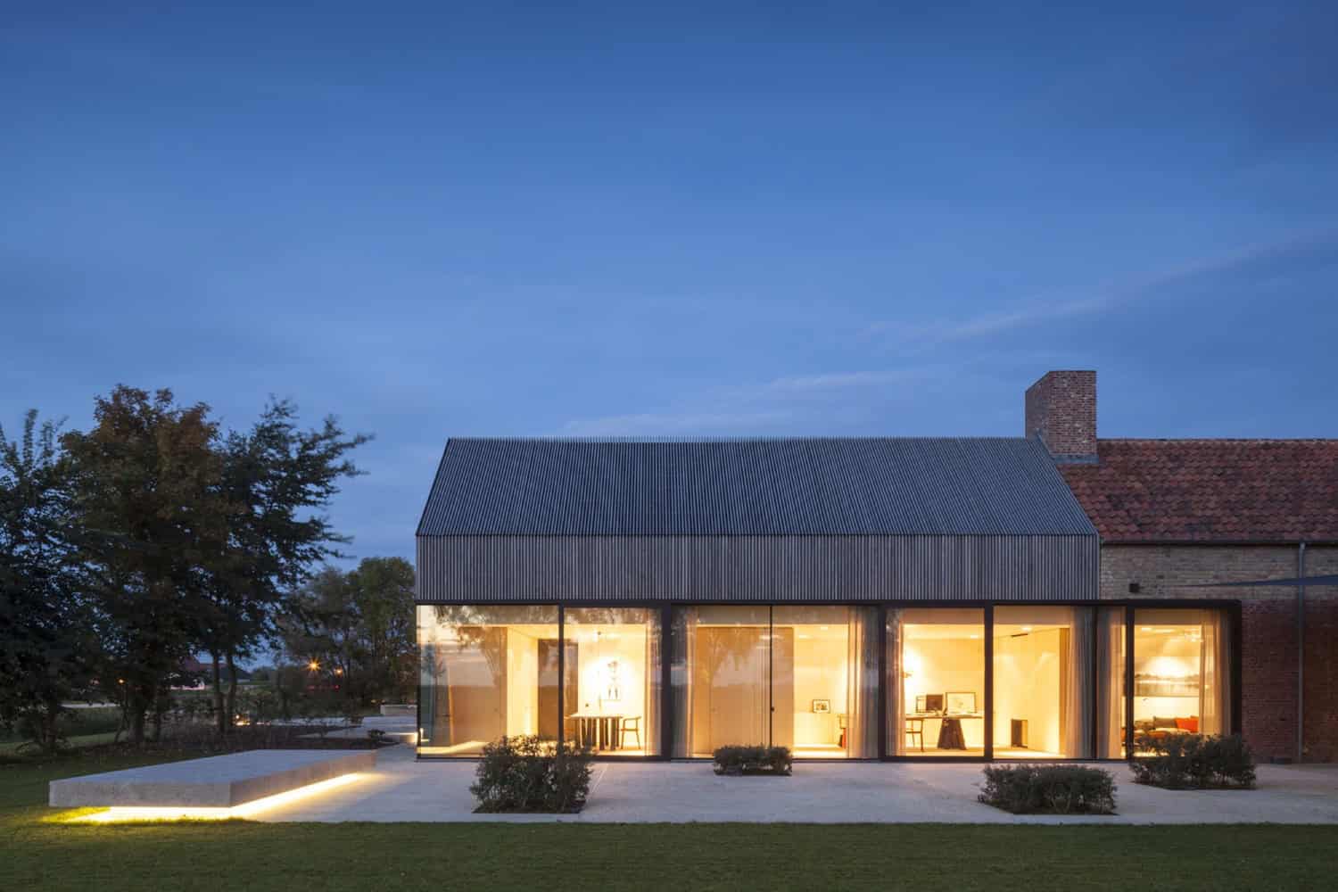 Contemporary glass extension blending modern architecture with traditional brick house, featuring large windows, minimalist design, and warm interior lighting, ideal for modern architectural home designs.